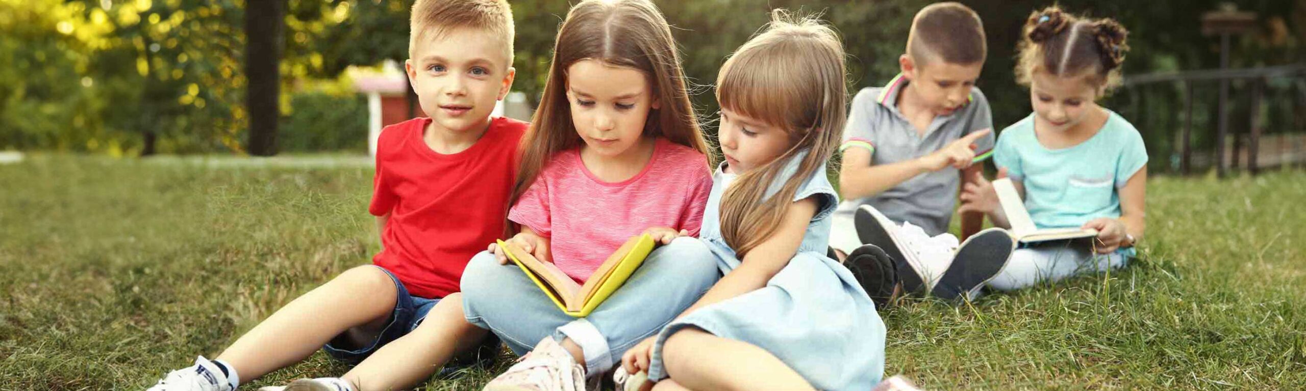 A group of young children reading outdoors.