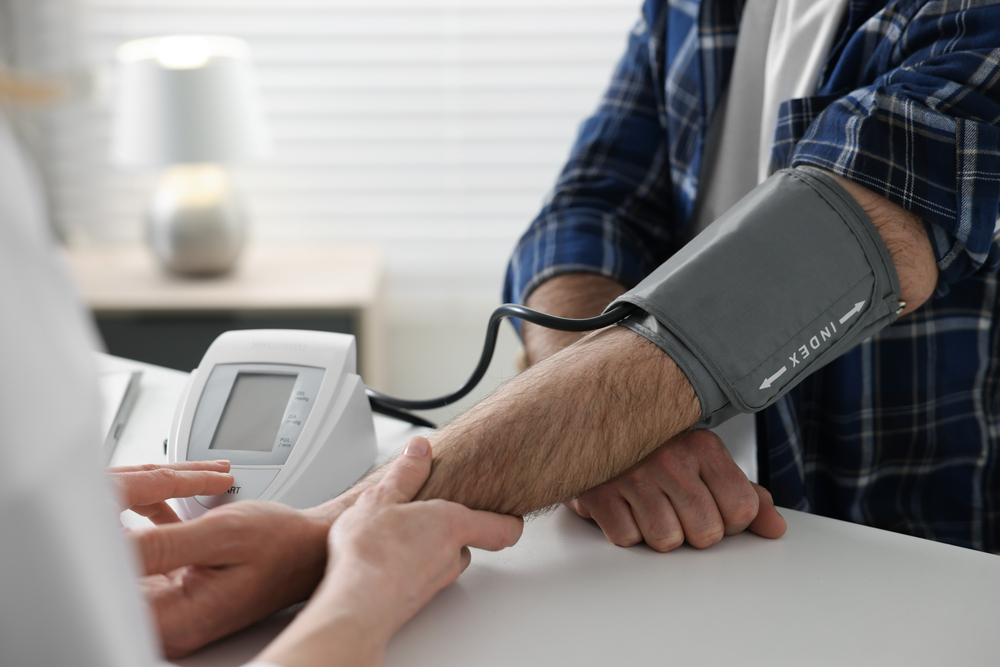 Doctor measuring blood pressure of man at table indoors, closeup